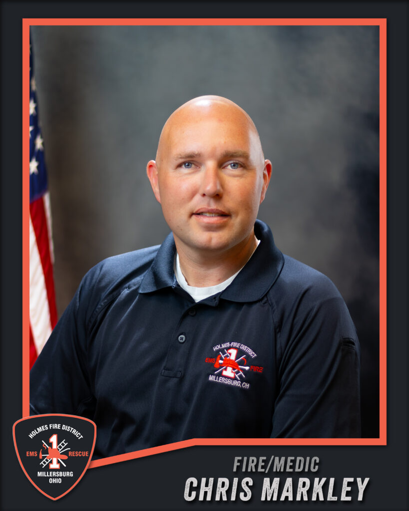 A man in a navy polo with a fire department logo poses for a formal portrait. An American flag is in the background. Text reads, “Fire/Medic Chris Markley, Millersburg, OH Fire District.”.
