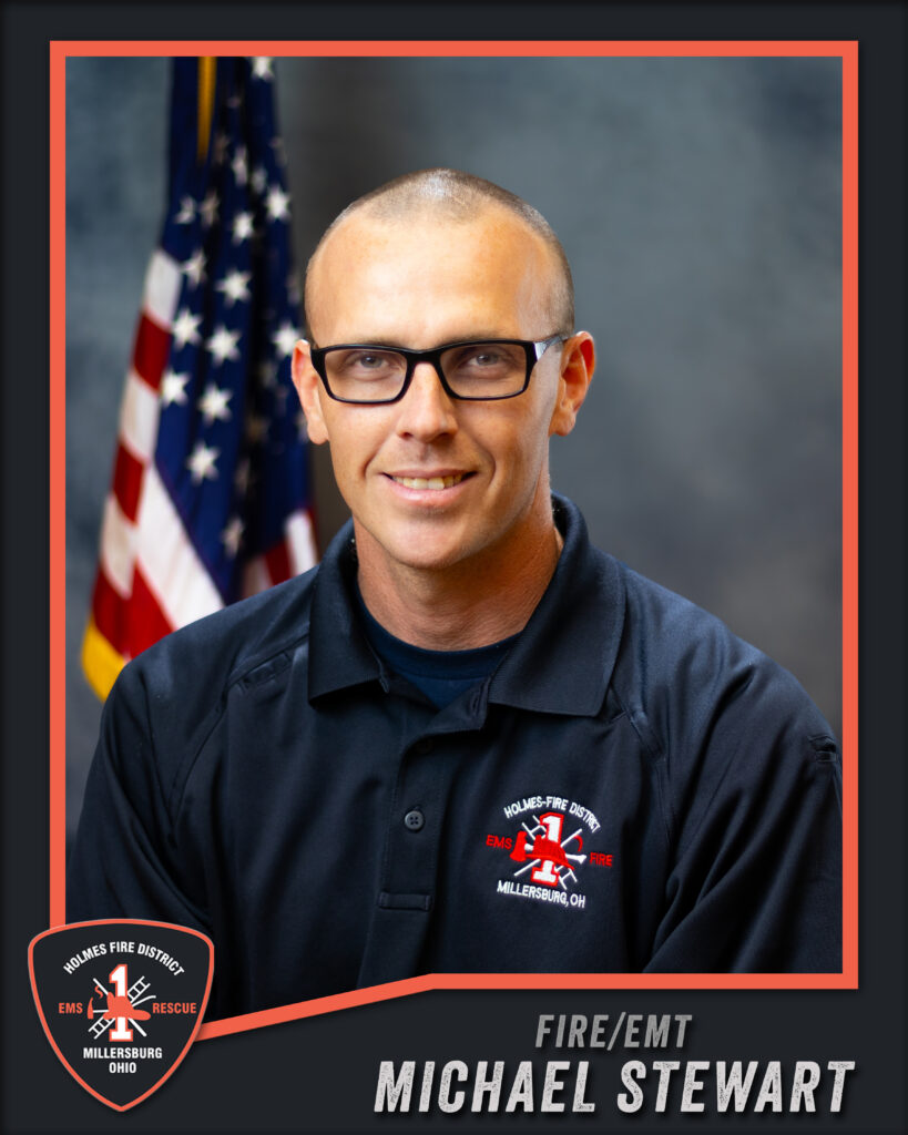 A man in glasses and a black uniform with a fire department logo sits in front of an American flag. The text reads “Michael Stewart, Fire/EMT, Holmes Fire District, Millersburg, Ohio.”.