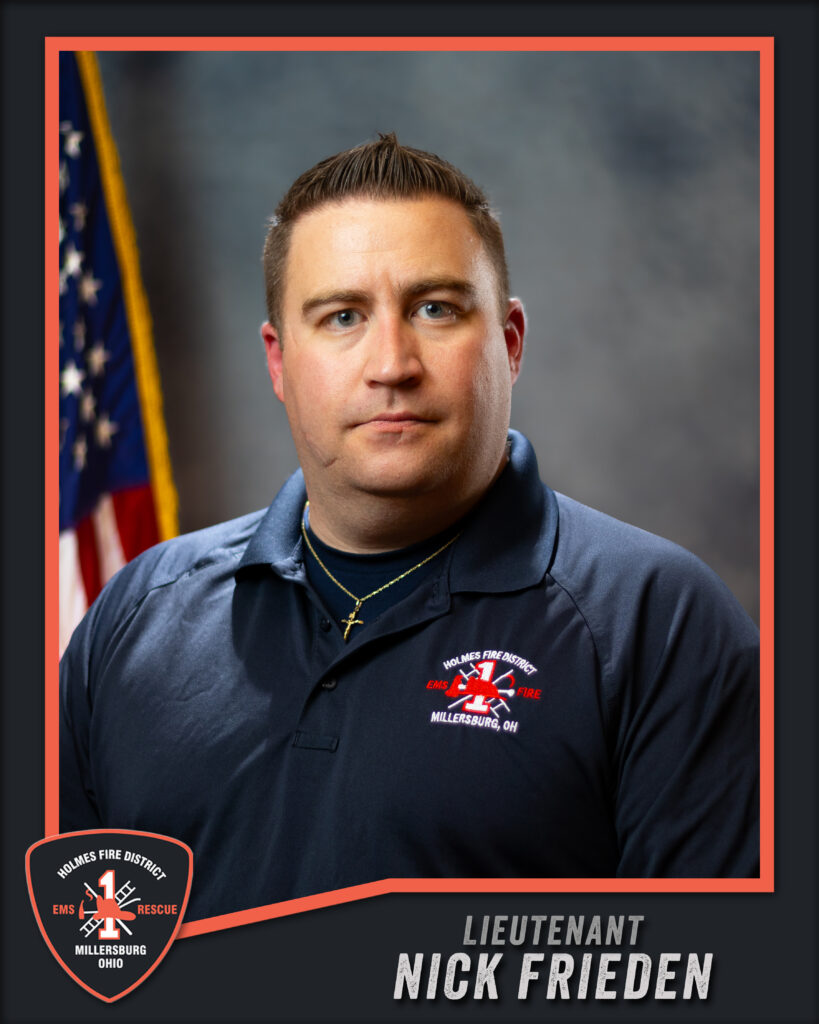 A man in a navy uniform shirt with an embroidered fire department logo poses in front of an American flag. Text at the bottom reads “Lieutenant Nick Frieden, Holmes Fire District, Millersburg, Ohio.”.