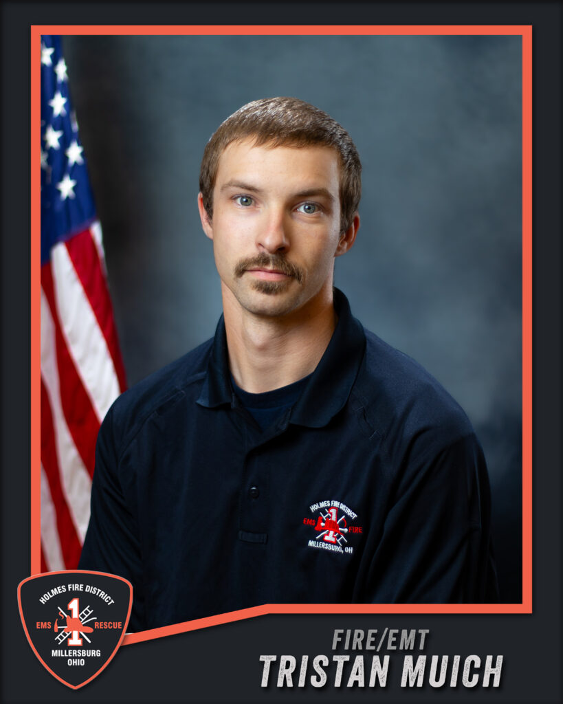 A man with short brown hair and a mustache poses in front of an American flag, wearing a dark Holmes Fire District shirt. Text on the image reads “FIRE/EMT TRISTAN MUICH” and displays the department’s badge.