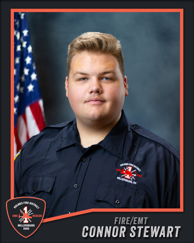 A uniformed firefighter/EMT stands in front of an American flag. The uniform displays the Holmes Fire District logo. Text at the bottom reads, “FIRE/EMT Connor Stewart.”.